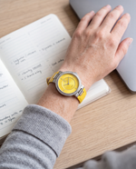 Clicöt Aphrodite 36mm watch in yellow and silver on a woman's left wrist, everyday lifestyle photo
