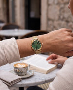 Close-up of the Clicöt Hera 36mm watch in green and gold on a woman's left wrist