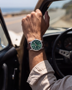 Clicöt Hermes 41mm watch in green, brown and silver on a man's left wrist, everyday lifestyle photo
